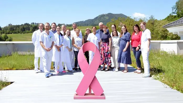 Rund 15 Ärzte, männliche und weibliche, stehen hinter einer rund einen Meter großen pinken Schleife