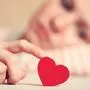Sad girl is holding heart symbol by her finger and looking at it. Love and relationships concept
