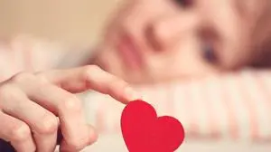 Sad girl is holding heart symbol by her finger and looking at it. Love and relationships concept