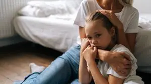 Portrait of sad little girl looking at camera and loving caring mother comforting offended afraid child daughter, showing love and care, expressing support, hugging and stroking hair sitting on floor.