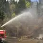 Man sieht einen Feuerwehrwagen und Einsatzkräfte, die auf einer Straße versuchen Wasser spritzen