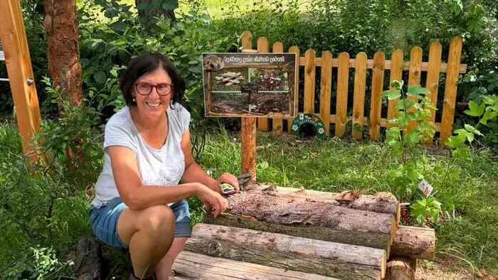 Eine Frau hockt vor einem Igelversteck in einem Garten und lächelt in die Kamera