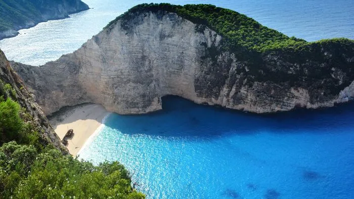 Navagio Beach, Zakynthos.Einer der schönsten Strände Griechenlands ist ohne Zweifel der Navagio Beach auf der Ionischen Insel Zakynthos. Die kleine Bucht wird auch Schmugglerbucht genannt: Zur Piraten- und Abenteuerfilm-Atmosphäre tragen die bis zu zweihundert Meter hohen Felswände bei, die den kleinen Strand umrahmen. Passend ist auch der Name der Bucht – Navagio bedeutet übersetzt „Schiffswrack“. Erreichbar ist das idyllische Strandparadies nur mit dem Boot. Infos unter: Mouzenidis Travel