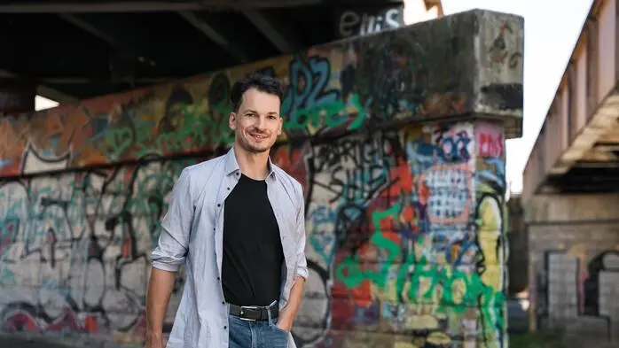 Ein junger Mann geht unter einer Brücke mit Graffiti und hält ein Buch in der Hand