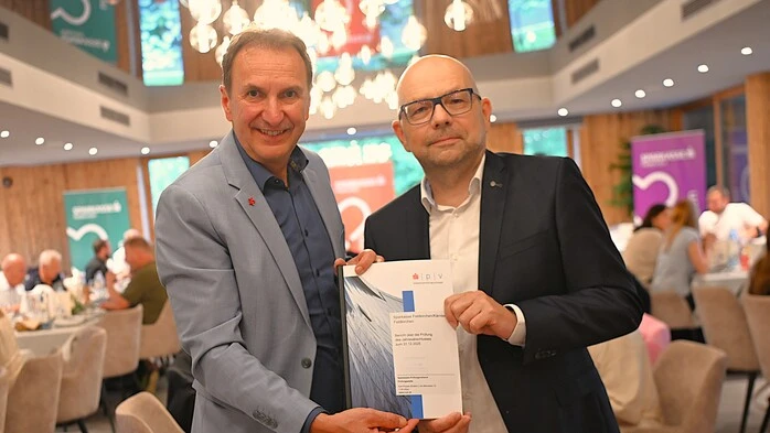 Zwei Männer im Anzug blicken in die Kamera und halten eine Broschüre