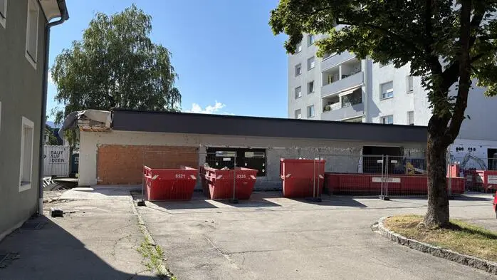 Außenansicht eines ebenerdigen Gebäudes, dass umgebaut wird. Im Hintergrund sieht man einen in die Höhe ragenden Wohnblock