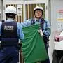 Zwei Polizisten in Tokio. Einer schaut her und hält eine grüne Matte in den Händen, den anderen sieht man von hinten.