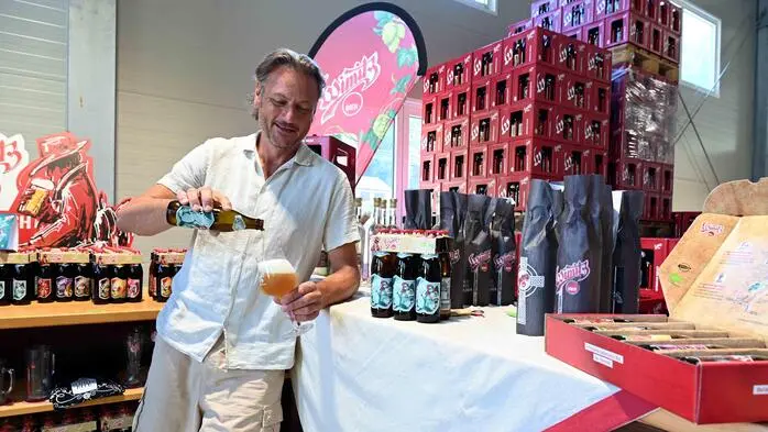 Ein Mitte-50-jähriger Mann schenkt sich ein Bier ein. Im Hintergrund sieht man Bierkästen und Bierflaschen.