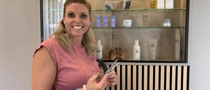 Eine junge Frau lächelt mit einer Schere und einem Kamm in der Hand in die Kamera