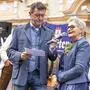 Zu sehen sind eine Frau und ein Mann auf einer Bühne. Der Mann hält der Frau ein Mikrofon hin, in das die Frau hineinspricht.