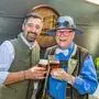 Zwei Männer in Tracht lachen in die Kamera und prosten sich mit einem Bier zu