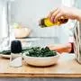 Close up woman adding olive oil while cooking kale chips or healthy salad for dinner on the kitchen table. Healthy eating, dieting lifestyle. Selective focus, copy space