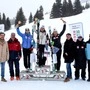 Personen stehen auf und neben Siegerpodest; Schnee im Hintergrund; Frauen am „Stockerl“ mit Skiern