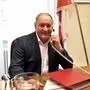 Ein 70 Jahre alter Mann sitzt hinter einem Schreibtisch und hält sich ein Festnetztelefon ans Ohr