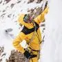 Ein Bergsteiger mit dicker gelber Winterjacke hängt in einer Wand und blickt nach oben.