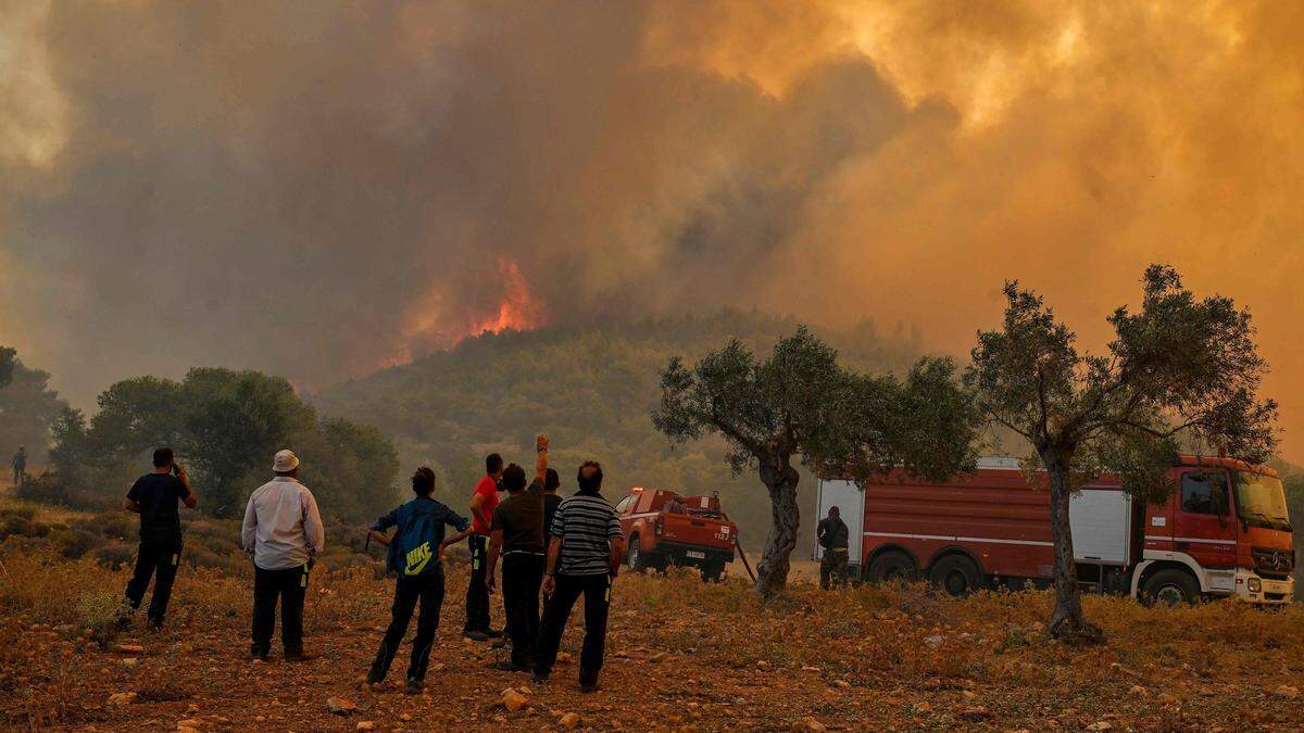 Menschen stehen vor einem Waldbrand in der Nähe von Athen