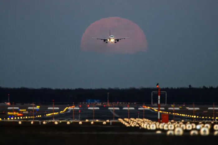 Ein Passagierflugzeug befindet sich am Frankfurter Flughafen im Landeanflug, während im Hintergrund der Vollmond aufgeht.