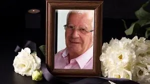 Ein Bilderrahmen mit einem Foto eines Mannes mit Brille, daneben liegen Fotos