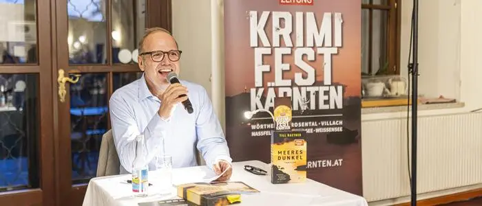 Ein Mann mit Brille sitzt an einem kleinen Tisch mit einem Buch und einem Mikrofon