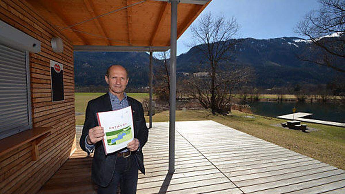 Bürgermeister Manfred Fleißner mit Plan des Radcampingplatzes, der im Bereich hinter ihm entstehen wird. Rechts ein Teil des Badesees 