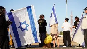 Israelis gather with national flags outside the Reim military base near the border with Gaza in southern Israel on October 13, 2025 to welcome the hostages about to arrive following their release by Hamas from the Gaza Strip. The Palestinian militant group was set to release all surviving Israeli hostages on October 13 in exchange for Palestinian prisoners held by Israel, as US President Donald Trump headed to the region for a peace summit having declared the war "over". Trump's lightning visit to Israel and Egypt aims to celebrate his role in brokering last week's ceasefire and hostage release deal -- but comes at a precarious time as Israel and Hamas negotiate what comes next. (Photo by Maya LEVIN / AFP)