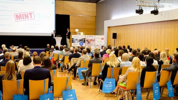 Viele Menschen sitzen in einem Raum und blicken auf eine Powerpoint-Präsentation