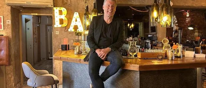 Ein Mann mit grauen Haar sitzt lässig auf einer Bar in einem Lokal