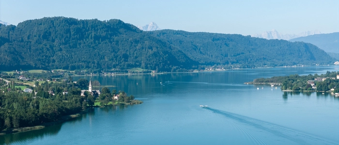 Eine Drohnenaufnahme eines blauen Sees unter blauem Himmel | Der Ossiacher See zählt zu einem beliebten Reiseziel