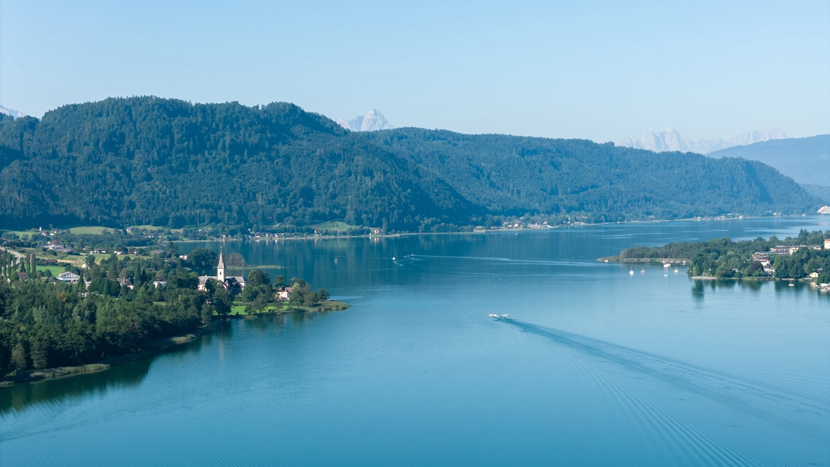 Eine Drohnenaufnahme eines blauen Sees unter blauem Himmel | Der Ossiacher See zählt zu einem beliebten Reiseziel 