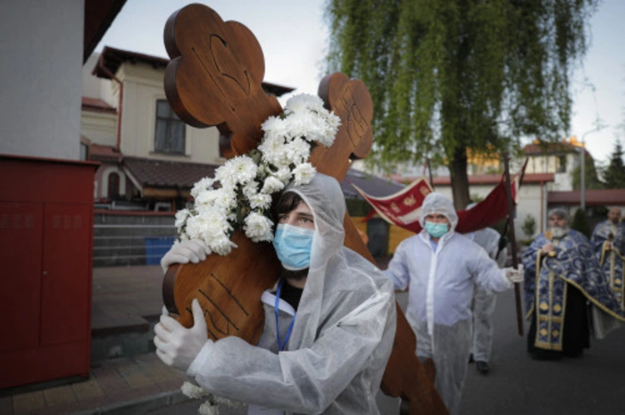 Ein Freiwilliger mit Schutzausrüstung trägt ein Kreuz, während er zusammen mit Priestern den orthodoxen Karfreitagsgottesdienstes in Bukarest begeht. 