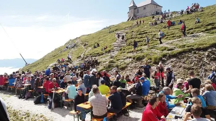 Zahlreiche Menschen auf einem Berg die auf Bierbänken sitzen