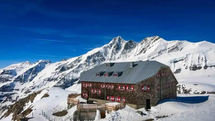 Eine hochalpine Hütte unter blauem Himmel und rundherum liegt Schnee