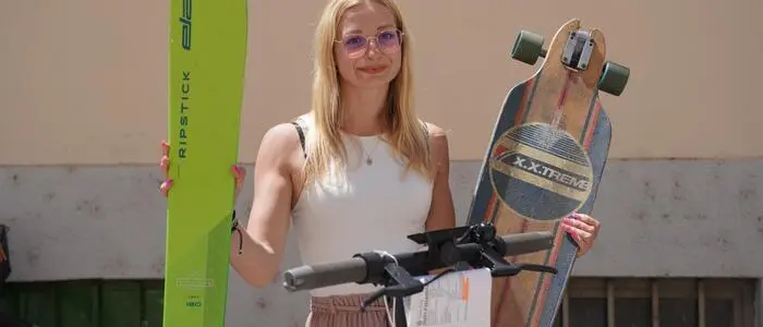 Eine junge Frau hält Ski und ein Skateboard hoch