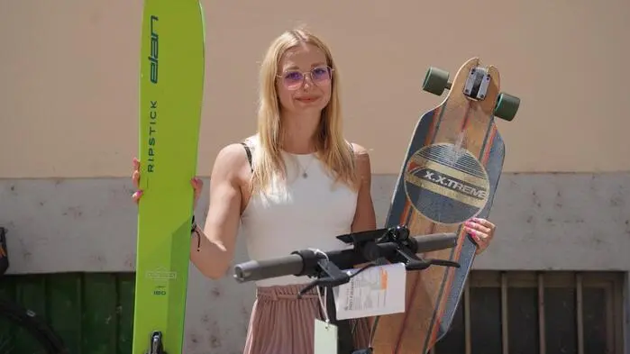 Eine junge Frau hält Ski und ein Skateboard hoch