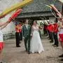 Ein Hochzeitspaar geht durch eine Hochzeitsgesellschaft, die sich links und rechts aufgestellt hat. Sie tragen Wasserrettungskleidung in rot und weiß