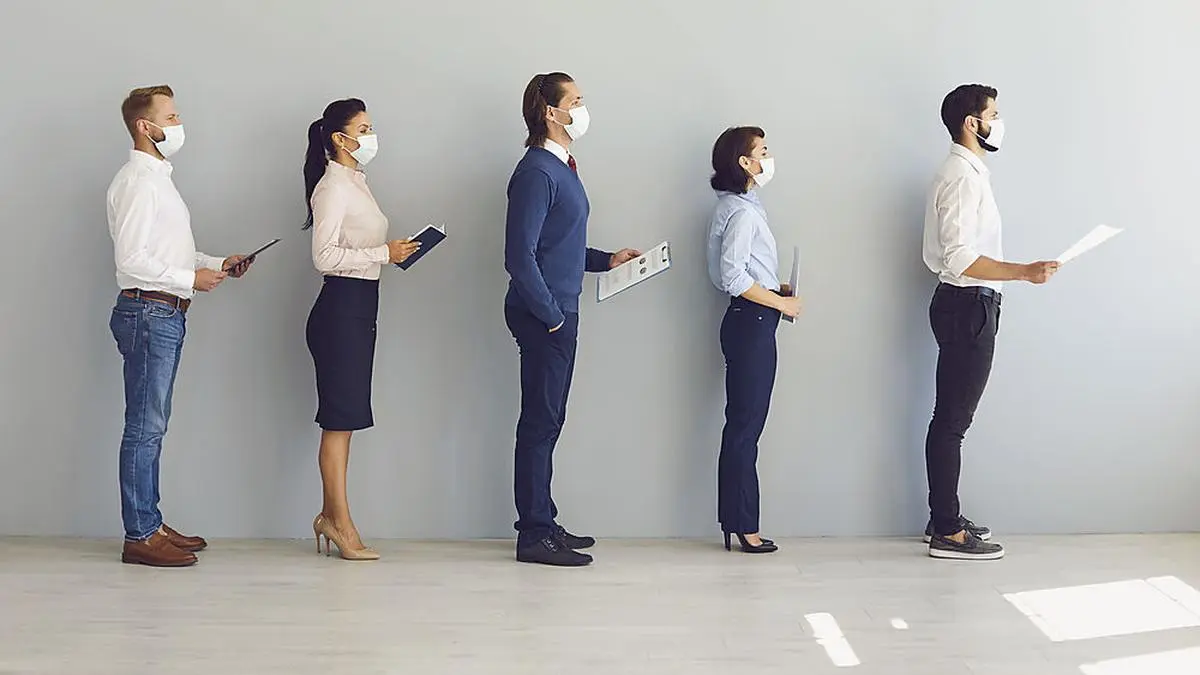 Job seekers wearing face masks standing in row keeping safe distance while waiting for job interview