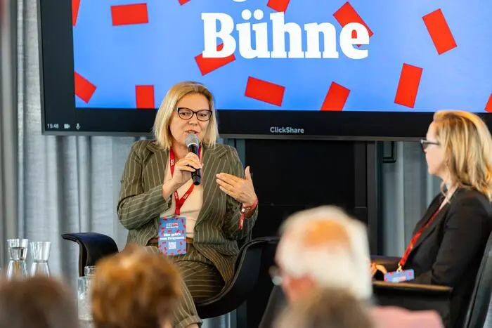 Kathrin Stainer-Hämmerle mit einem Mikrofon in der Hand, sitzt auf einer Bühne bei einer Veranstaltung der Kleinen Zeitung