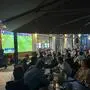 Viele Menschen sitzen in einem Gastgarten und verfolgen ein Fußballspiel im Fernsehen