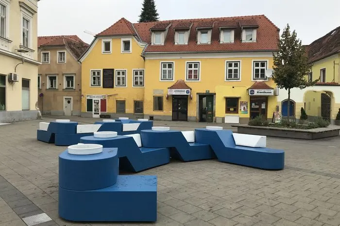 Entworfen wurde das Stadtmöbel vom Grazer Architekten Reinhold Tichon. Hergestellt wurde es vom Tischler Silverius Griessner, den den Prototypen in Zusammenarbeit mit der Ortweinschule Graz gefertigt hat.