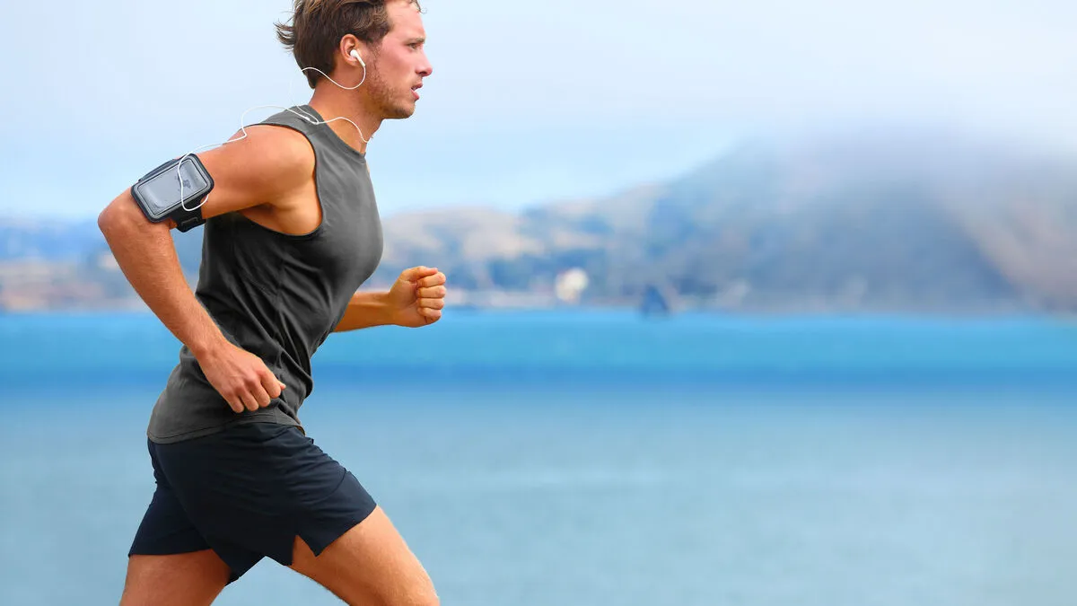 Running app on smartphone. Male runner listening to music jogging with armband for smart phone. Fit man fitness model working outdoor by water.