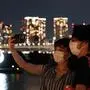 This picture taken on August 21, 2021 shows people taking pictures before the Paralympic Games symbol lit up at night on the Odaiba waterfront in Tokyo. (Photo by Charly TRIBALLEAU / AFP)