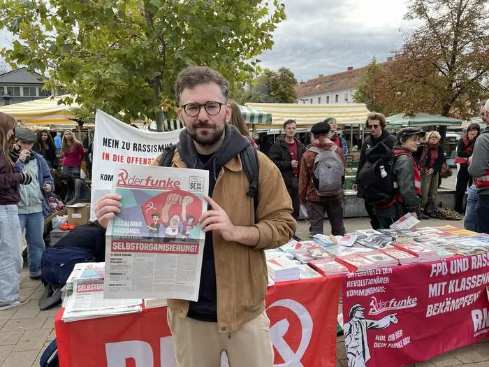 Christoph Pechtl steht vor dem Infostand der RKP und hält die Parteizeitung „Der Funke“ in Händen