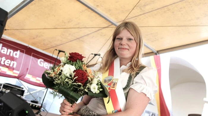 Zu sehen ist eine junge Dame mit Schärpe und einem Blumenstrauß