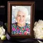 Ein Bilderrahmen mit einem Foto einer Frau mit weißen Haaren und buntem Kleid, nebenan liegen weiße Blumen | Gerlinde Mayer hinterlässt vier Kinder, zehn Enkelkinder und acht Urenkel