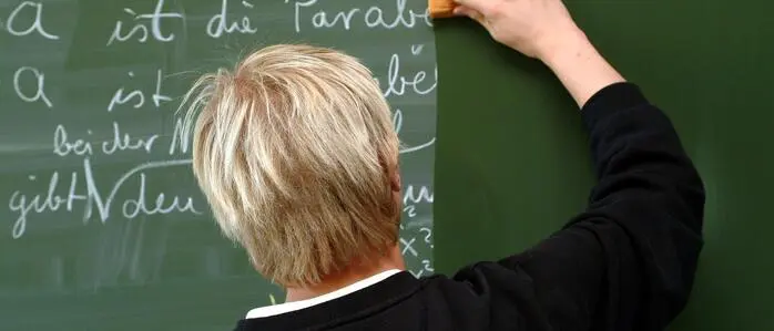 Das Bild zeigt einen Lehrer, der die Tafel putzt