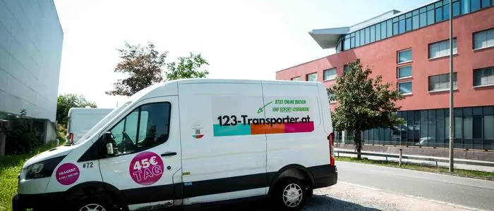 Man sieht einen weißen Kastenwagen mit der Aufschrift von 123-Transporter auf einem Parkplatz in einer Stadt stehen | Die Fahrzeuge von 123-Transporter sind in Österreich mittlerweile nicht mehr zu buchen