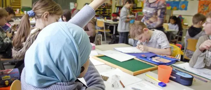 Das Bild zeigt ein Mädchen mit einem Kopftuch in einem Klassenzimmer