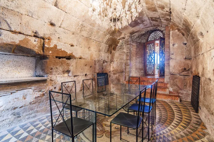 Die “Appia Antica” entlanglaufend, könnte niemand ahnen das sich hinter diesen Mauern mit drei Toren, das “Paradies” verbirgt. Carlo Ponti hatte die Angewohnheit seine Gäste durch das bescheidenste der drei Tore zu empfangen, von dem aus er ihnen ein Zimmer aus römischer Zeit präsentierte, mit Fassaden und Gewölbe aus Tuffstein und dem mit Mosaiksteinen überzogene Fußboden in Form eines Medusenkopfes, welcher heute noch existiert.