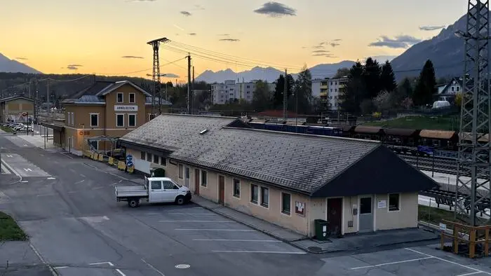 Seitliche Vogelperspektive eines flachen Gebäudes neben einem Gleis, davor steht ein Lieferwagen