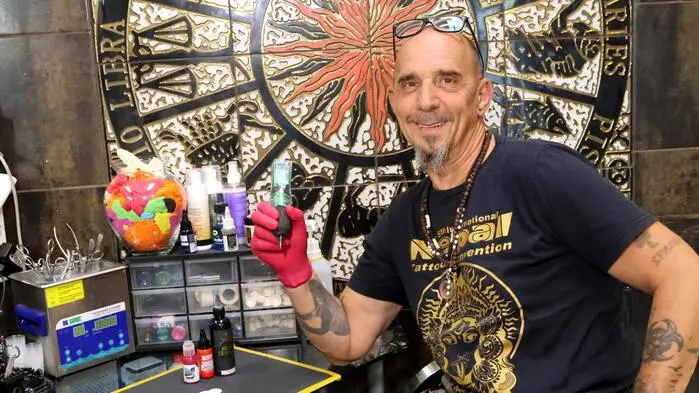 Ein Mann mit Glatze in einem Tattoostudio. Er hält eine Nadel in der rechten Hand.